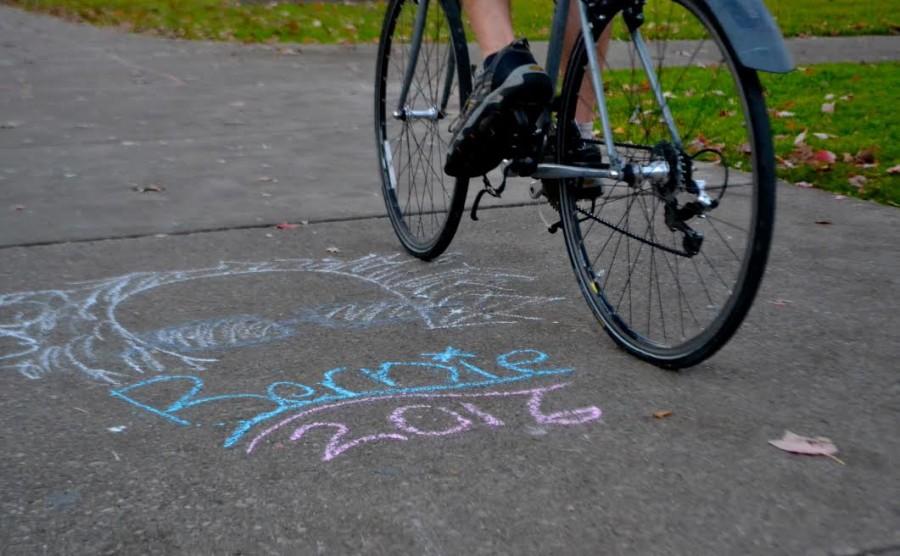 Outline of Sanders in The Diag while a biker takes a glance at the political sidewalk chalk. 