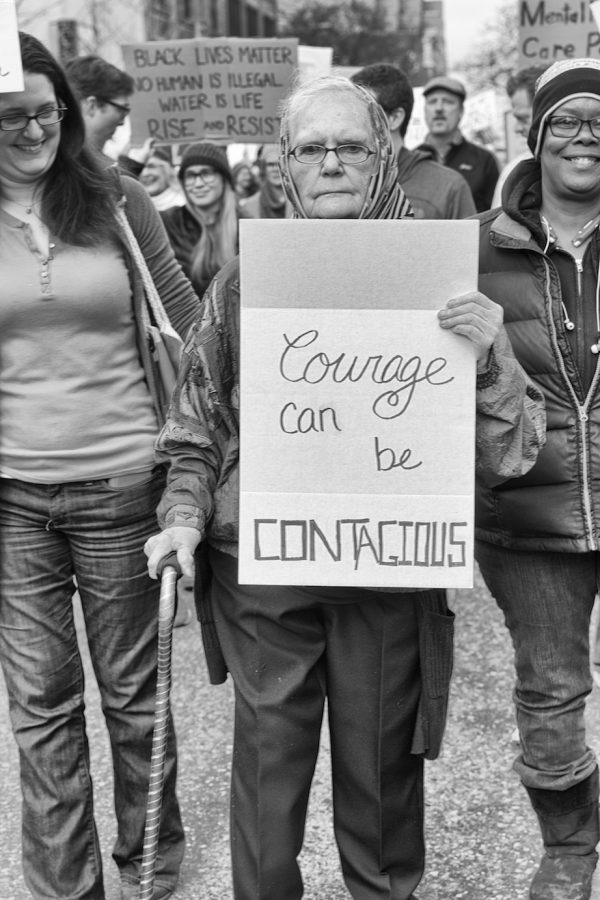 A women holds a sign that reads, courage can be contagious.