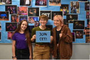 Community Ensemble Theatre members pose in front of Craft Theater with a sign reading Join CET!. The auditions for the groups fall play will take place on Sept. 12-13.