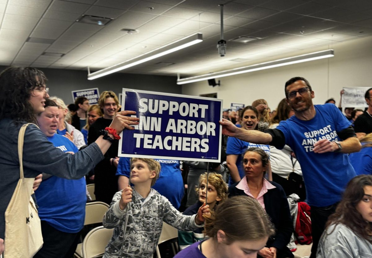 AAPS community members gather together, raising signs and wearing t-shirts in solidarity. The board meeting commenced with chants from the crowd in support of teachers. We are teachers, we are not the problem. community members chanted.
