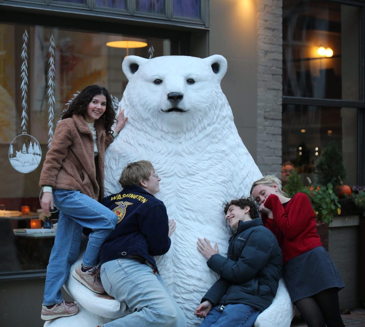 Toula Greenawalt (top left), Gwen Galvin (bottom left), Malcolm London (bottom right) and Claire Lewis (far right) huddle around the bear statue next to Sava's restaurant downtown. 