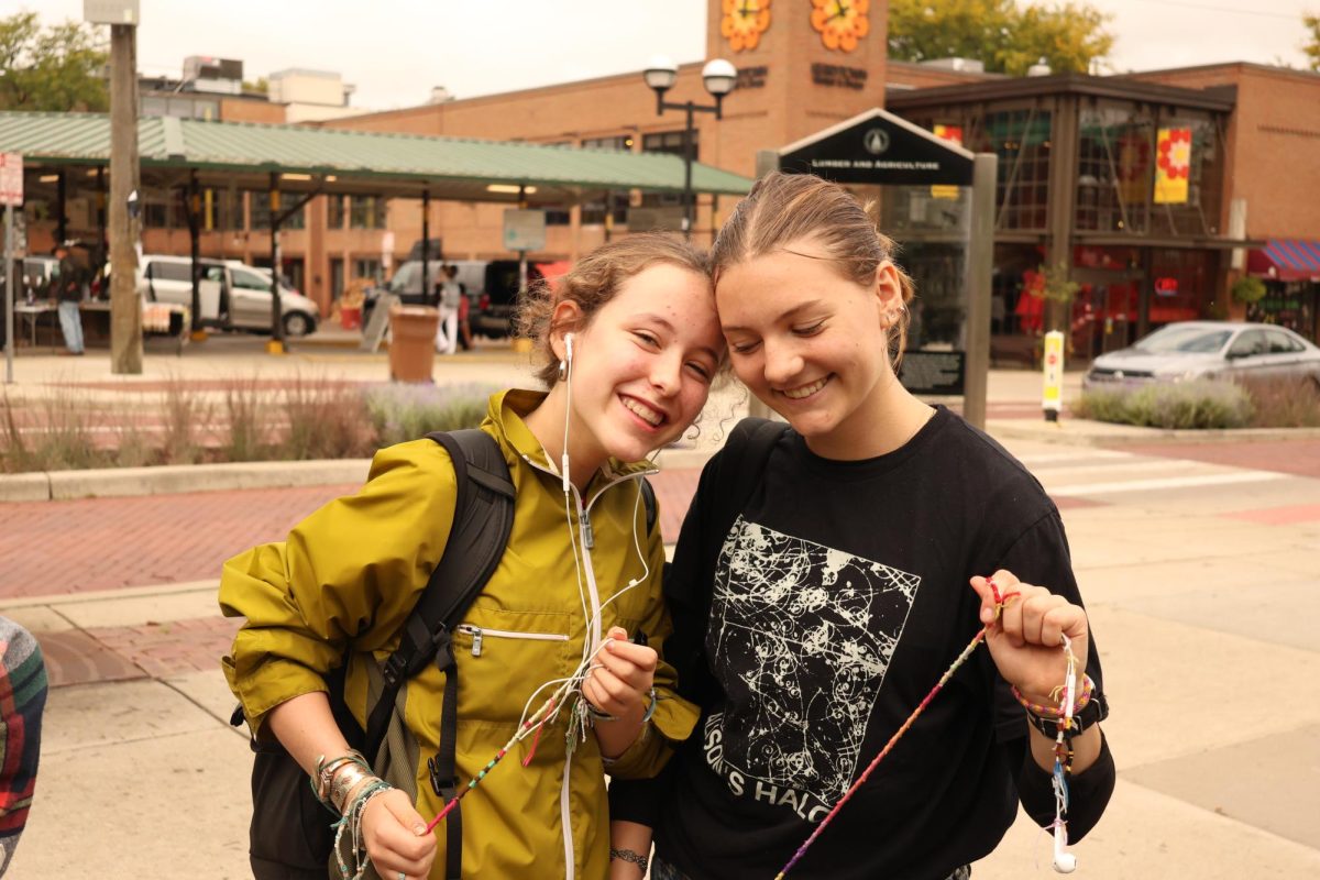 Sadie Jacobson poses with her friend Ani Ledbetter, another threaded earbuds enthusiast, in the Kerrytown market area. Jacobson had been out walking around during her lunch block when she ran into her friend, and the two sat down together and talked about their collective stories about music and friendship bracelets. 