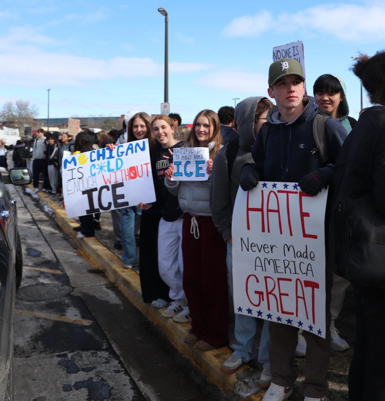 Pioneer students stand on the edge on the sidewalk holding signs out while cars pass by.