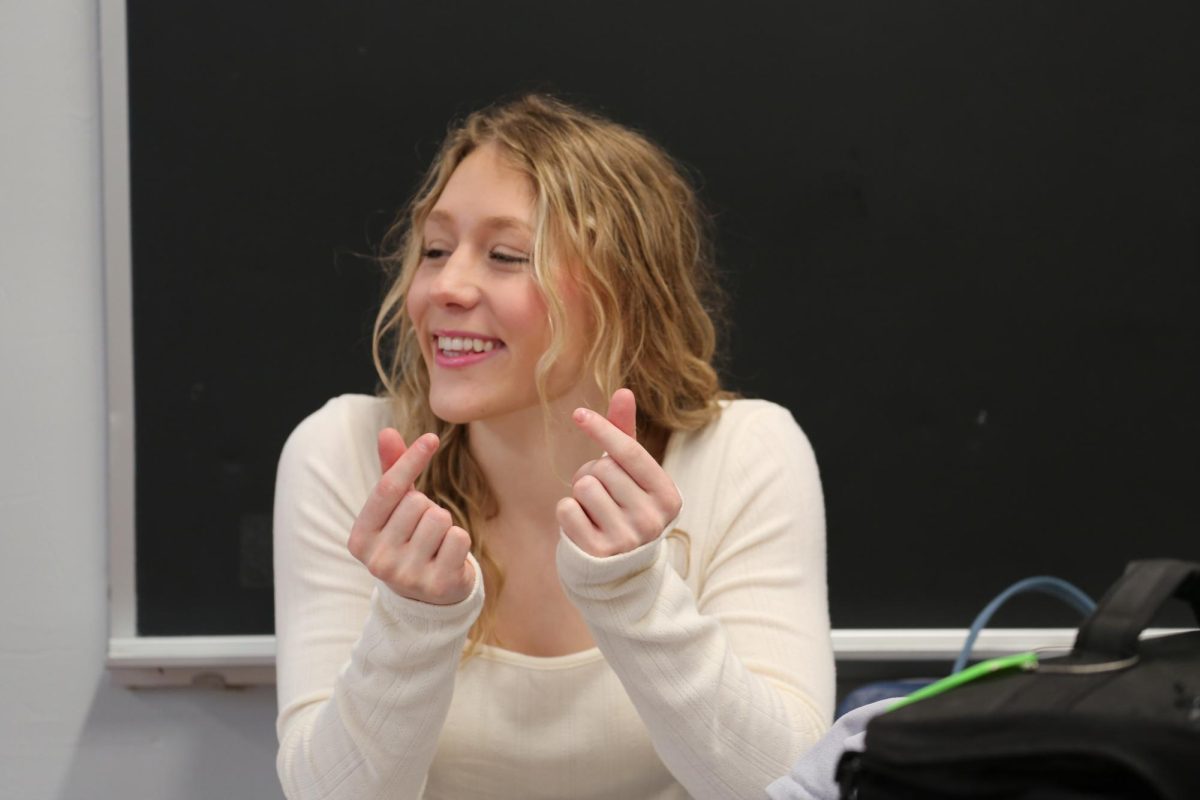 Adrienne Schadler makes heart-shaped hand gestures as students walk through the hallway. On the Thursday before Valentines Day, Schadler decided to spread love and smiles to her peers to celebrate the holiday. "I was in a really good mood today and just excited for Valentines," Schadler said. "I love making the heart hands at people, sometimes they think it's funny or don't know what it means."